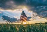 Scott Grice standing proudly beside a sheriff’s badge emblem with a sunset over Pine County farmland
