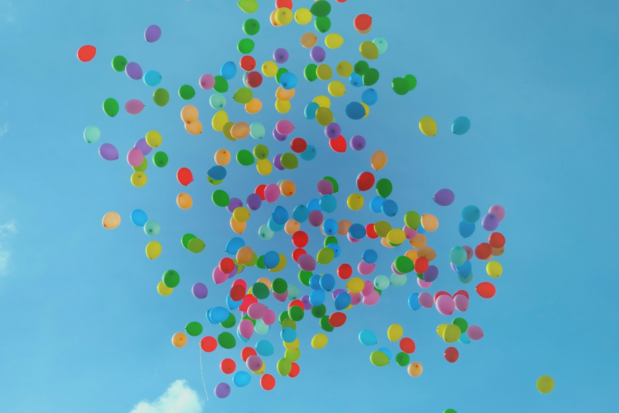 A large mass of balloons are released into the blue sky