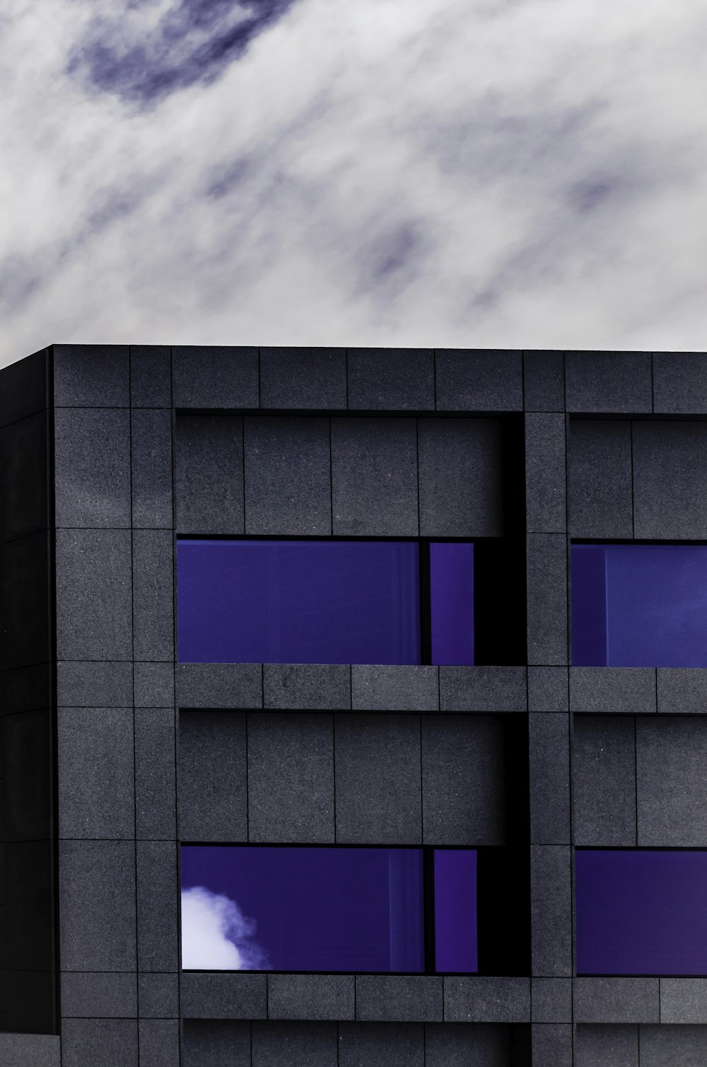 bâtiment en béton gris et violet sous ciel nuageux