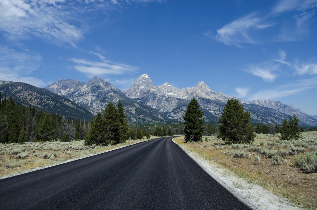gray asphalt road under blue sunny sky, Black road along the mountains