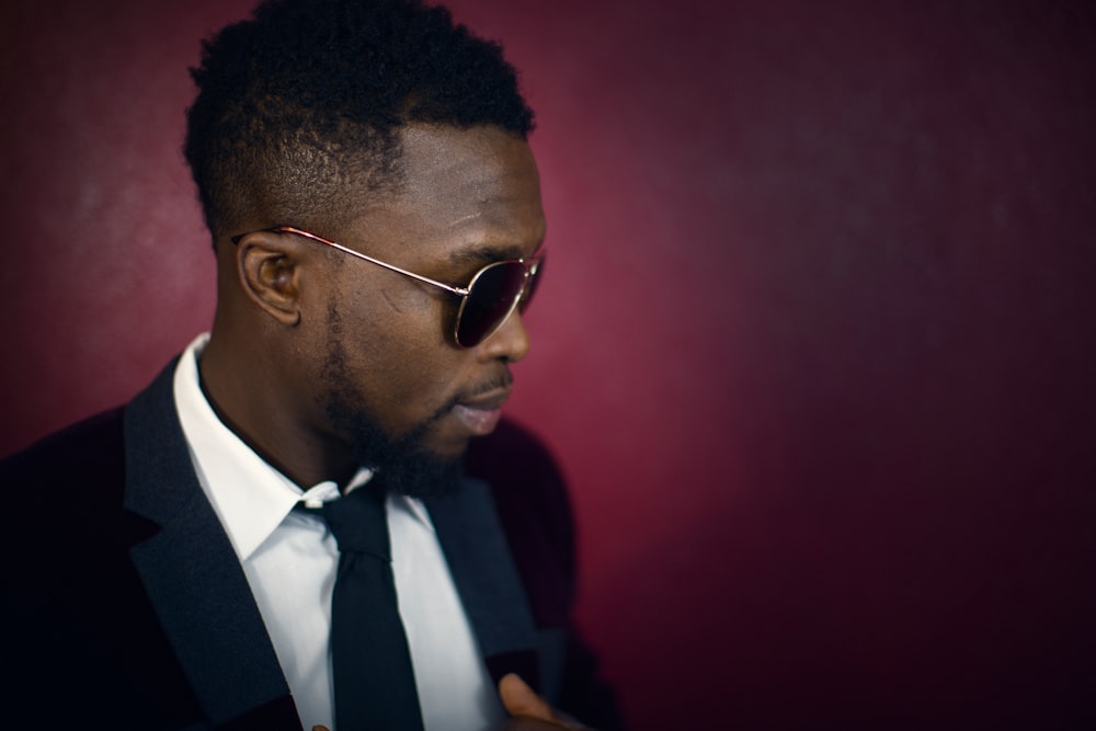 An elegant man in sunglasses against the backdrop of a dark red wall