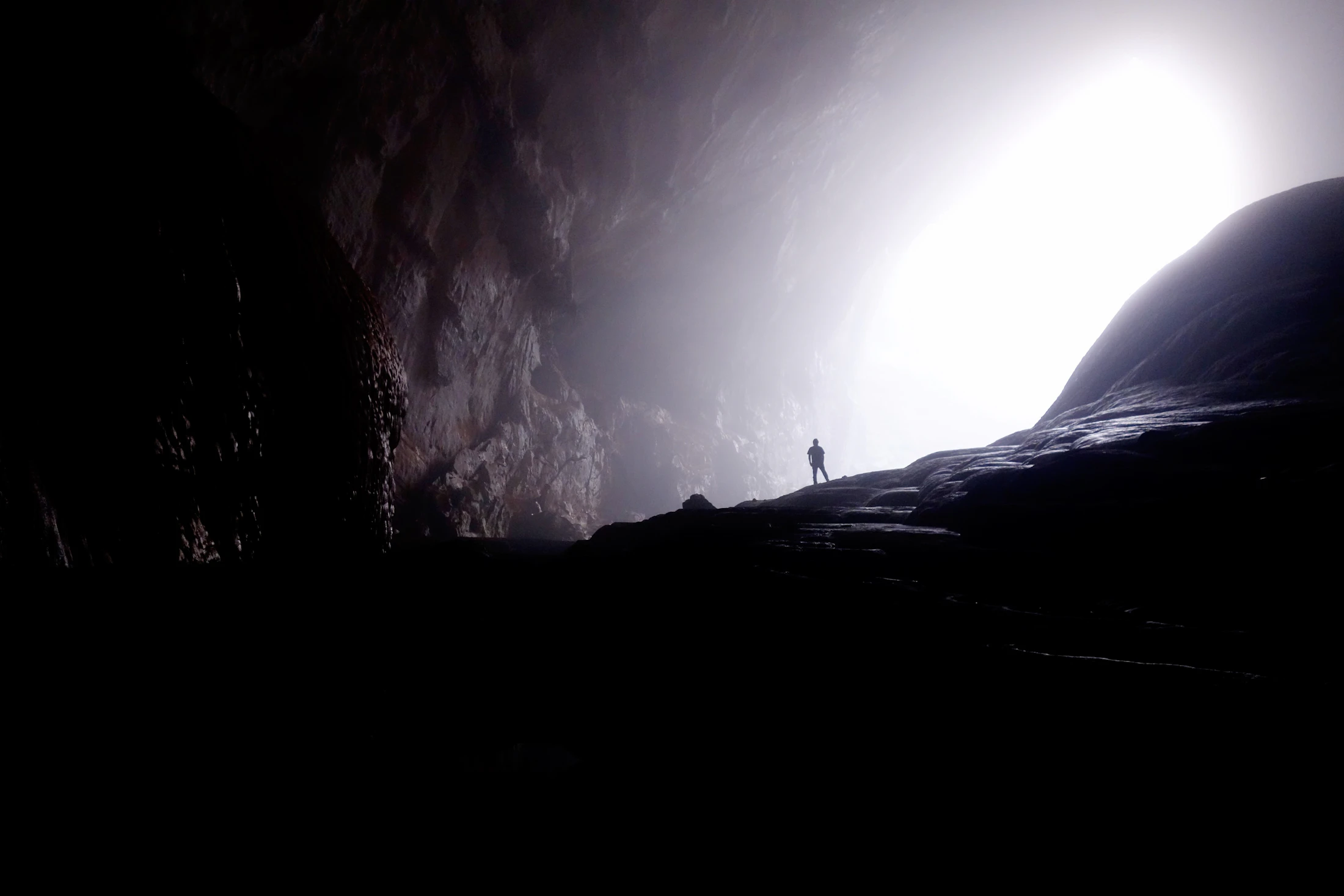 Silhouette au cœur d’une immense grotte ouverte sur la lumière.