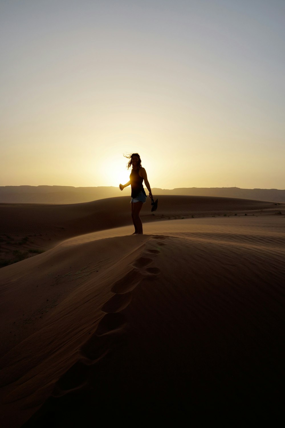 femme debout sur le sable pendant le coucher du soleil