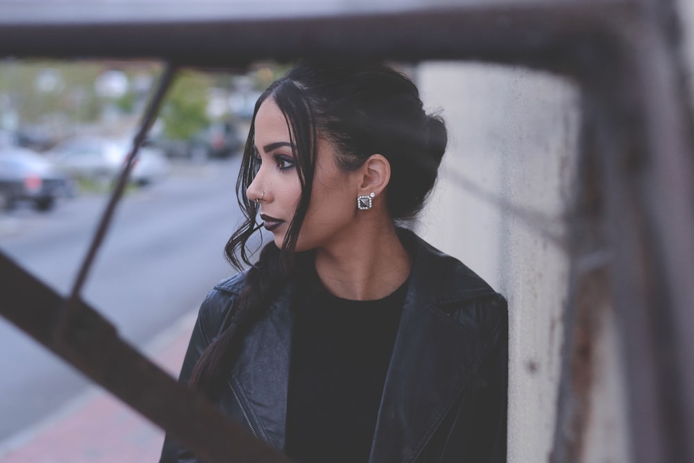 Fashionable woman with dark makeup and hair leaning against a wall
