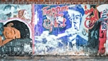 A colorful graffiti mural on a brick wall, featuring illustrated figures and bold text in both English and Arabic. The artwork includes a woman in a headscarf and a colorful, abstract representation of a man. The words 'The return of the spirit' are prominent in the center.