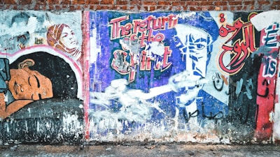 A colorful graffiti mural on a brick wall, featuring illustrated figures and bold text in both English and Arabic. The artwork includes a woman in a headscarf and a colorful, abstract representation of a man. The words 'The return of the spirit' are prominent in the center.