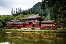 Japanese style temple near calm water behind mountain at daytime