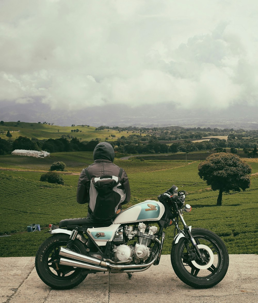 man sitting on motorcycle while facing broad green field