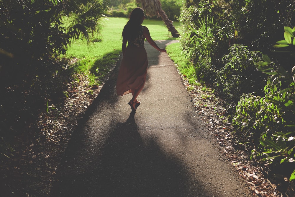 Femme en robe rose debout sur un trottoir en béton gris près de plantes vertes