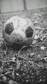 A close-up shot of an old, well-worn leather football resting on a grassy pitch at sunset.