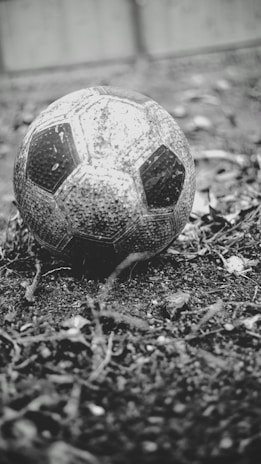 Close-up of a worn soccer ball resting on the grass at sunset.