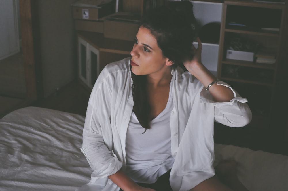 woman sitting on bed touching her hair inside room