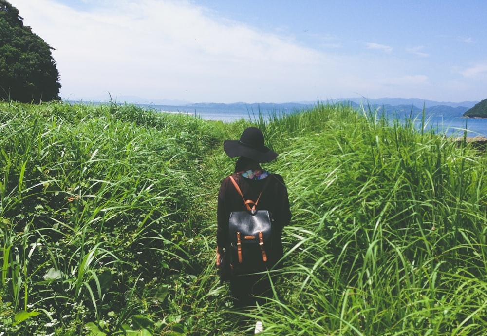 woman standing in the middle of green grass near sea at daytime