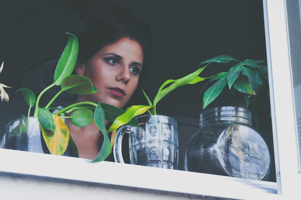 A woman staring out a window with plants on the sill.