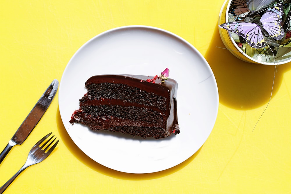 sliced chocolate moist cake in plate near gray stainless steel fork and knife