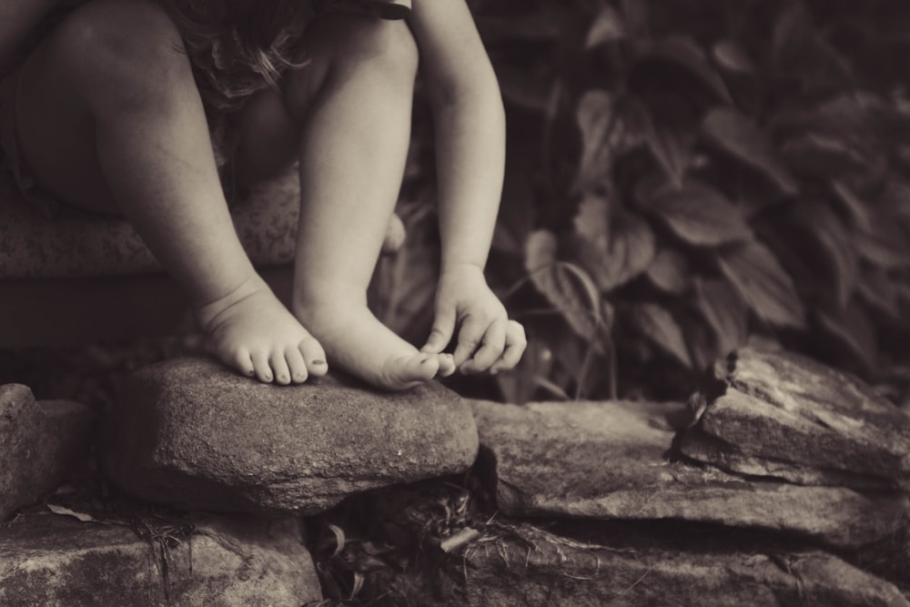 depth photography of child sitting on rock beside plant