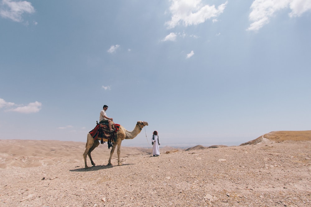 People ride a camel through the dry desert sand of Kfar Adumim