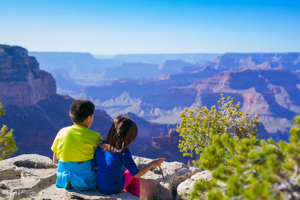 boy sitting beside girl in blue shirt near green leafed tree