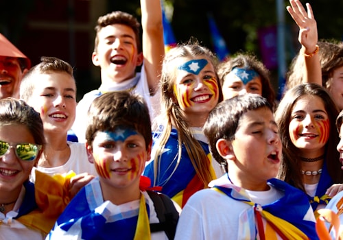 A group of young people are gathered together, several with painted faces in blue, yellow, and red colors. They are smiling and appear to be enjoying themselves. Flags or similar paraphernalia are draped on their shoulders or held in their hands. The scene is bright and lively, set outdoors.