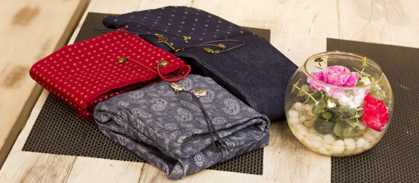 Flat lay of three kurtis in pastel shades arranged neatly on a rustic wooden table with fresh jasmine flowers.