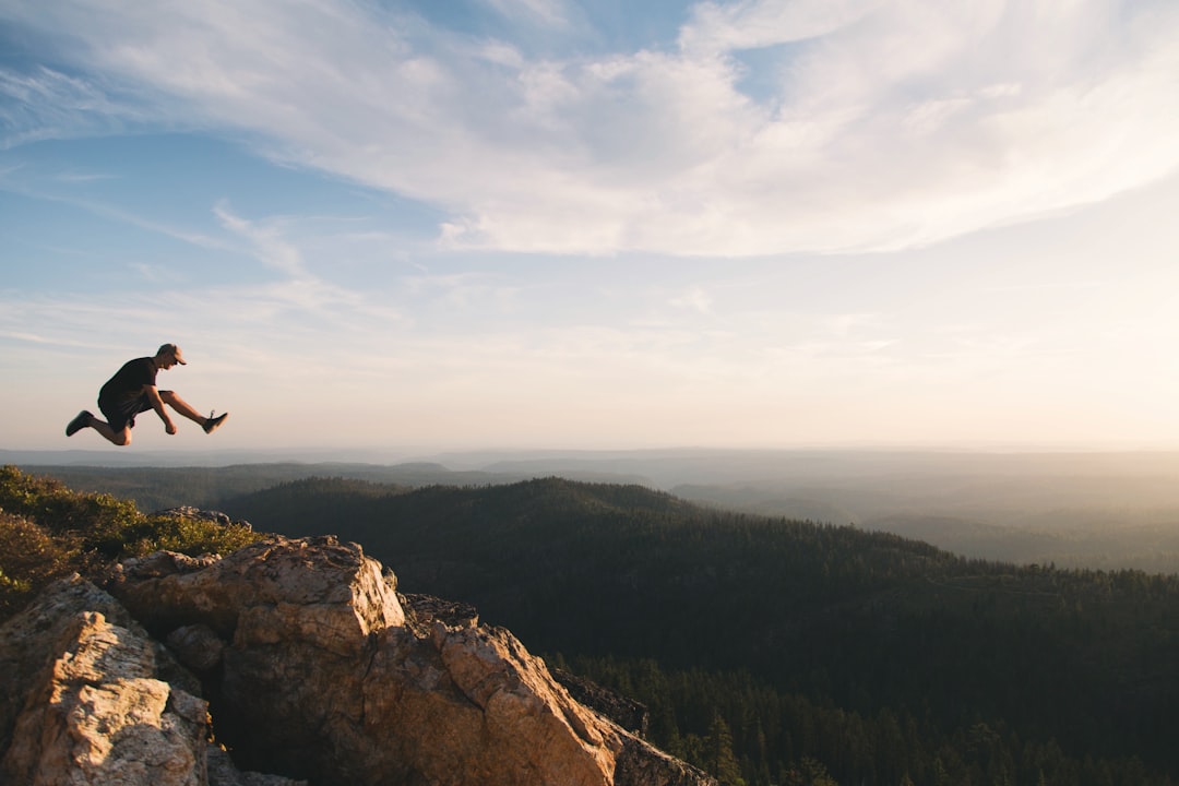 man jumping on brown rock mountain during daytime