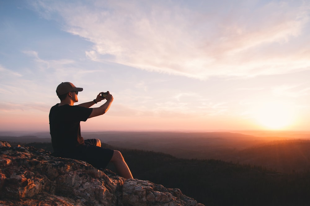 man sitting on mountain cliff taking picture