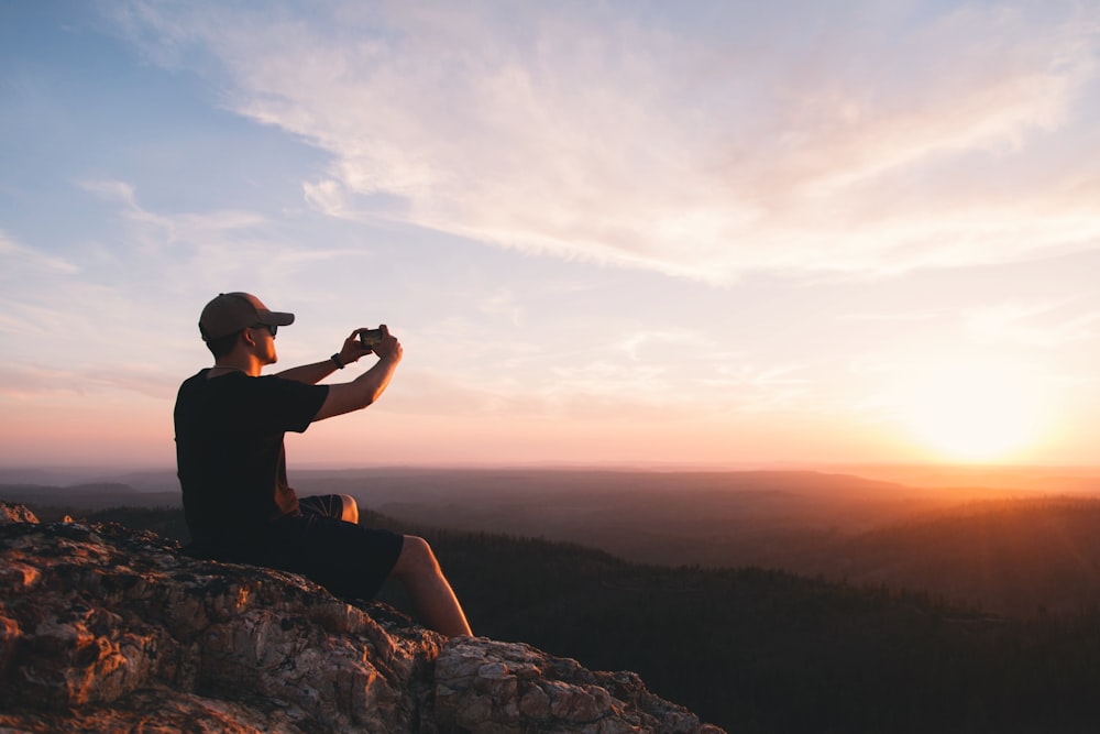 Mann sitzt auf Bergklippe und fotografiert