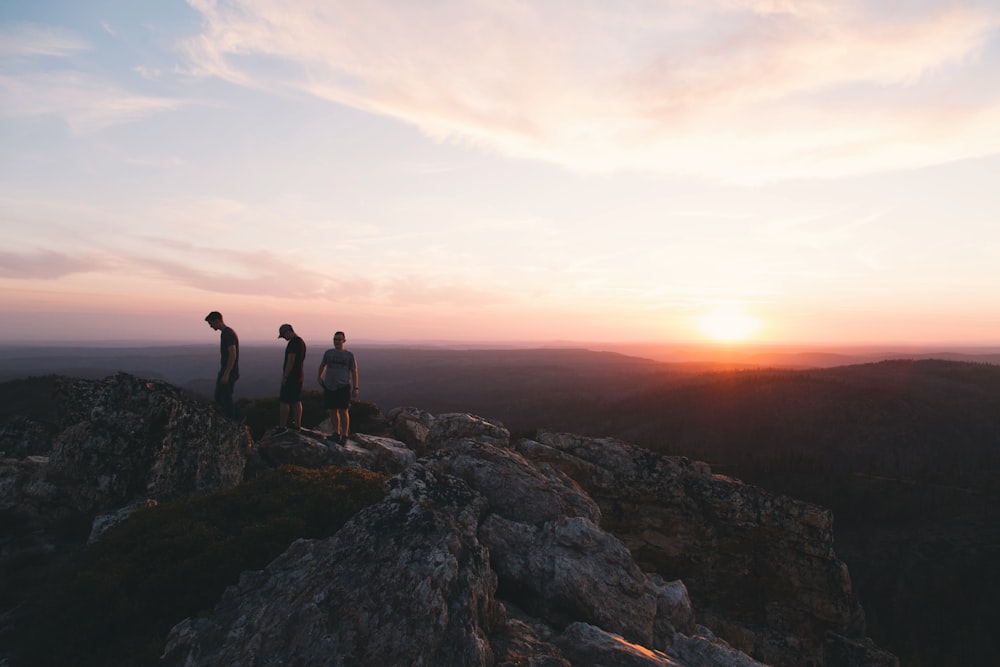 three person standing on mountain during daytime