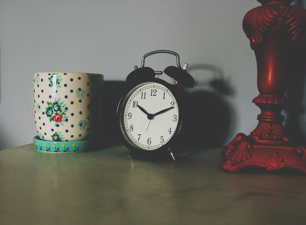 horloge de table noire à côté d’un vase en céramique