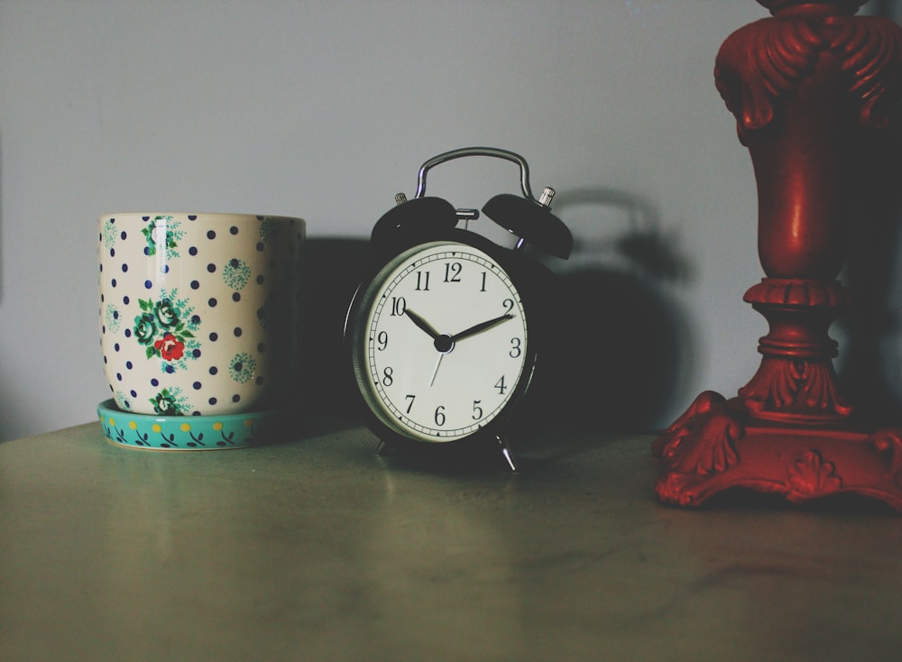 Reloj de mesa negro junto a jarrón de cerámica