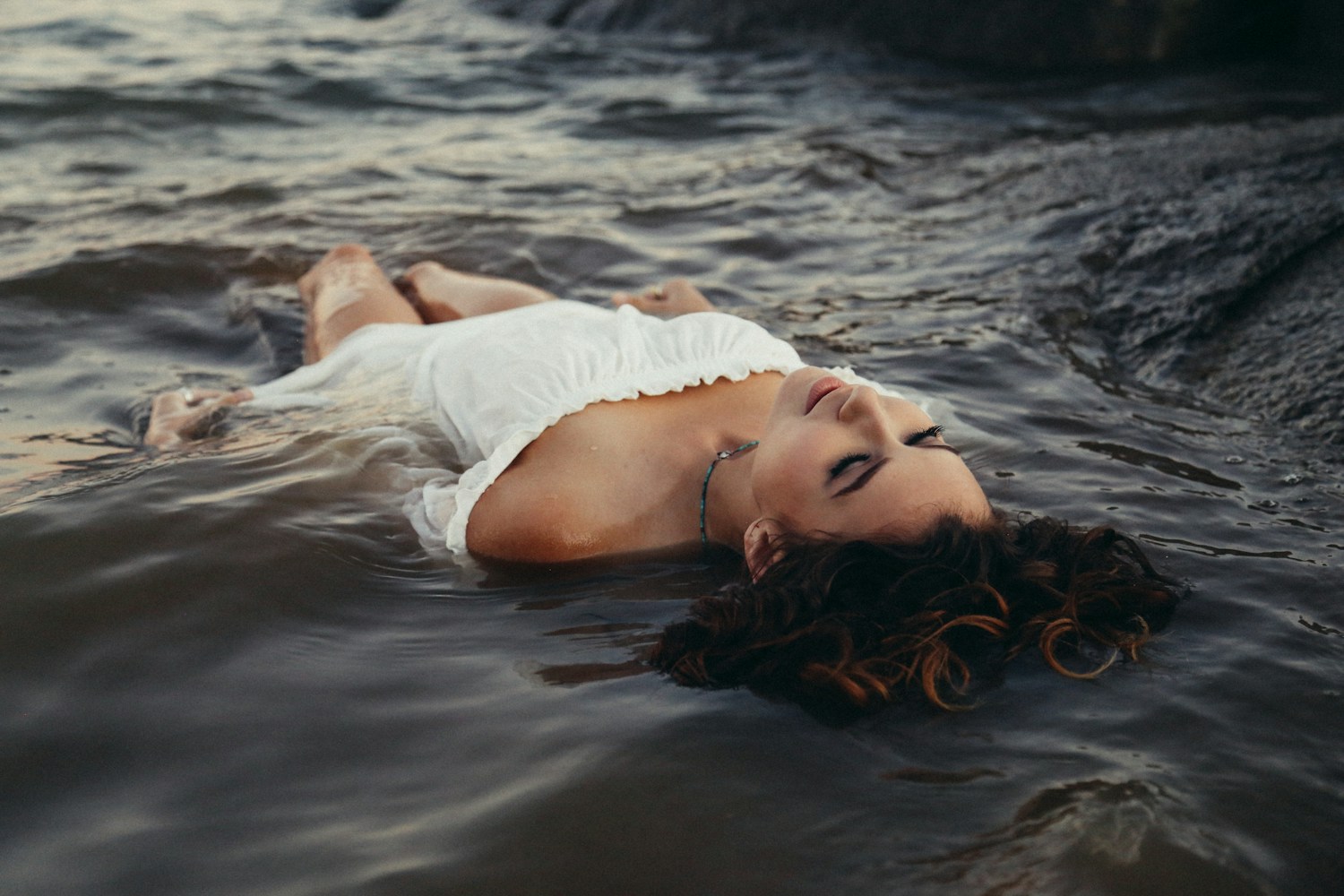 A woman in a white dress floating on her back in water.