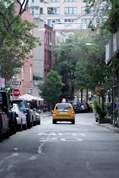 yellow taxi cab on gray concrete road top near buildings and trees during daytime