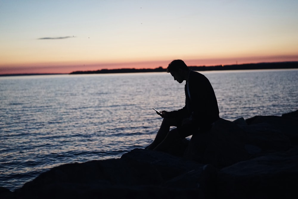 man sitting on rock in front of ocean