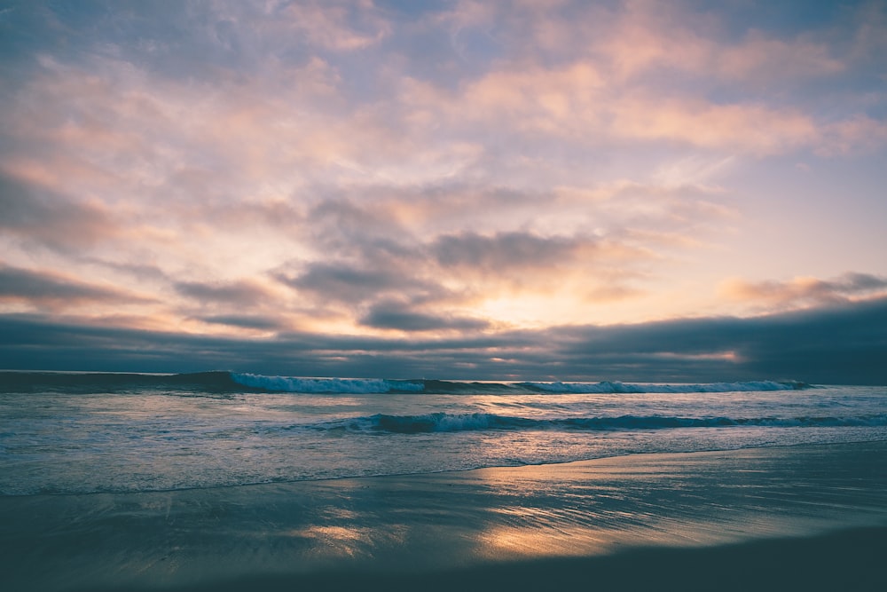 a sunset view of a beach with waves coming in