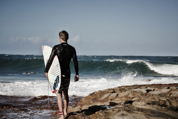 person holding surfboard near shore