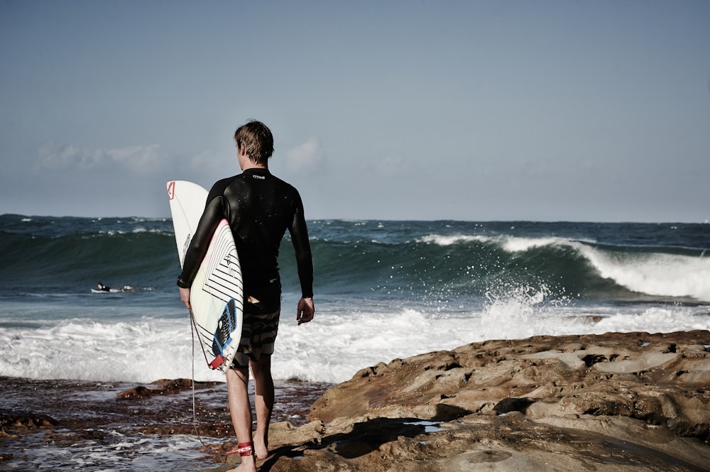 person holding surfboard near shore