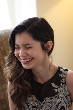 A candid shot of a woman laughing softly, wearing a flowing dress in a beige setting.