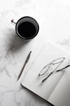 A neat desk with a cup of coffee next to an open book and reading glasses.