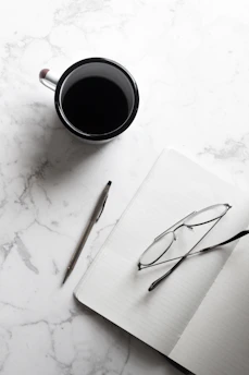 A compact crossbody bag placed on a marble table next to a cup of coffee and a notebook