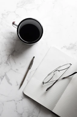 A neat desk with a cup of coffee next to an open book and reading glasses.