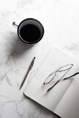 Flat lay of Gerald’s signature notebook, pen, and a cup of tea on a clean wooden desk.