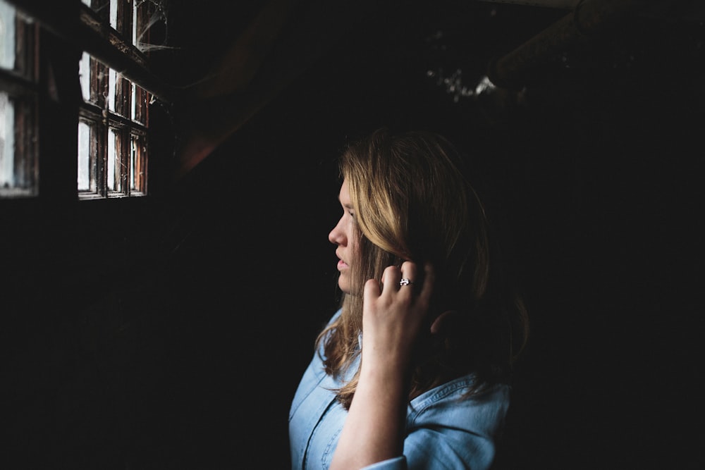 Woman with blonde hair wearing a blue shirt and ring looking out of a window covered in spider webs