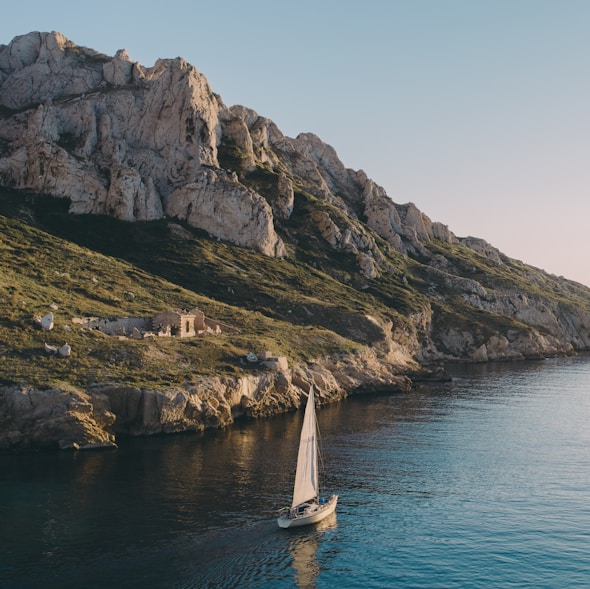 white sailboat near island rocks