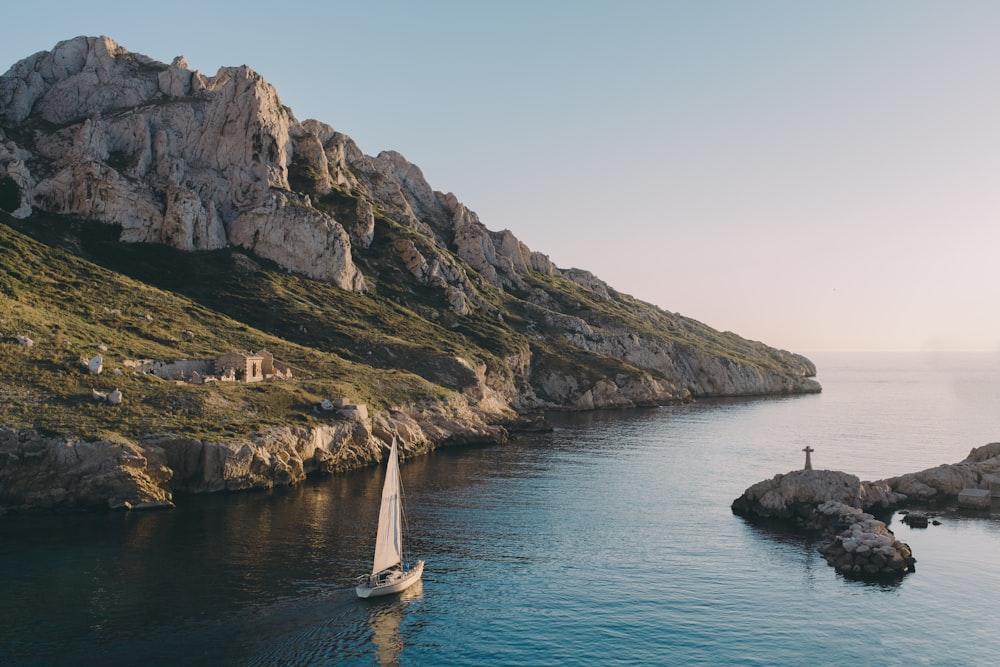 white sailboat near island rocks