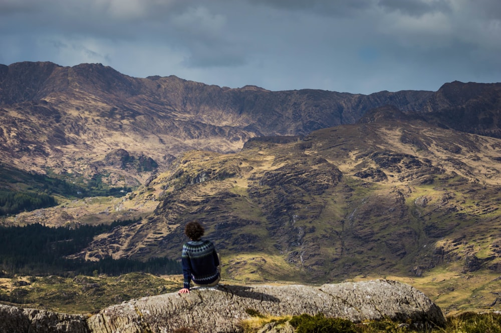 Persona sentada en una barrera de hormigón con vistas a la montaña durante el día
