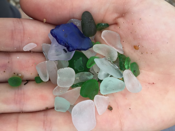 A delicate hand holding a piece of sea glass against the backdrop of a calm sea horizon.