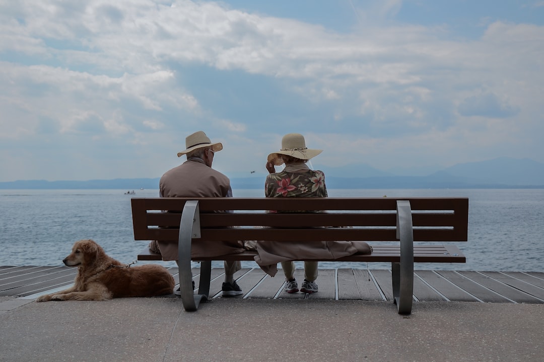 An older couple enjoy a seaside moment on a bench with their dog