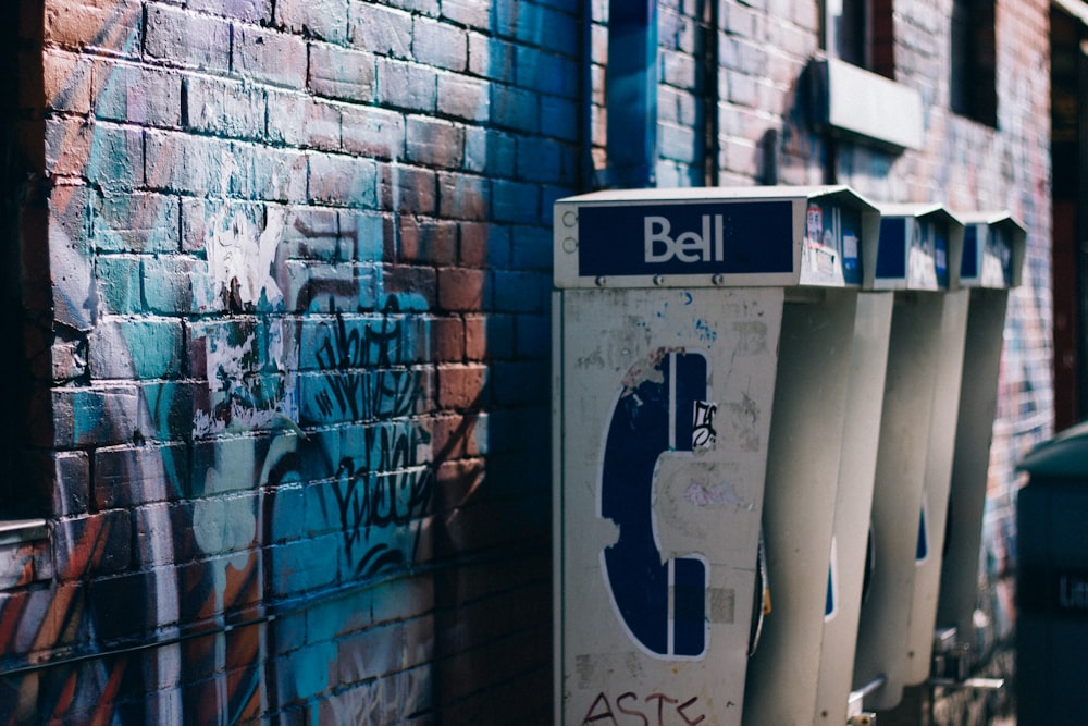 white and black Bell phone booth beisde concrete bricked wall with graffiti