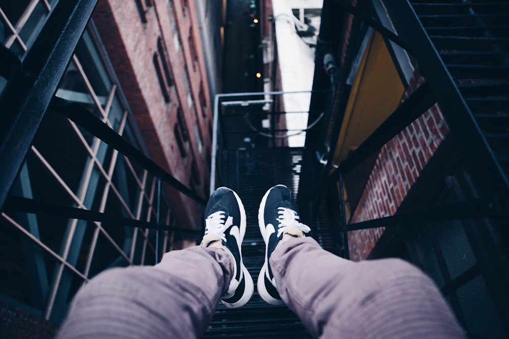 person wearing pair of black Nike shoes sitting on metal frame