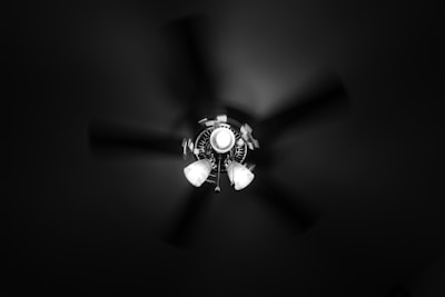 A ceiling fan is captured from below, with three light fixtures attached. The fan blades are blurred, suggesting motion, while the central light illuminates the surrounding area.